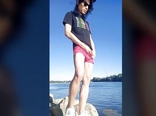 Twink boy with long dark hair pissing pee on the river dressed in glasses cap sneakers boxer tshirt